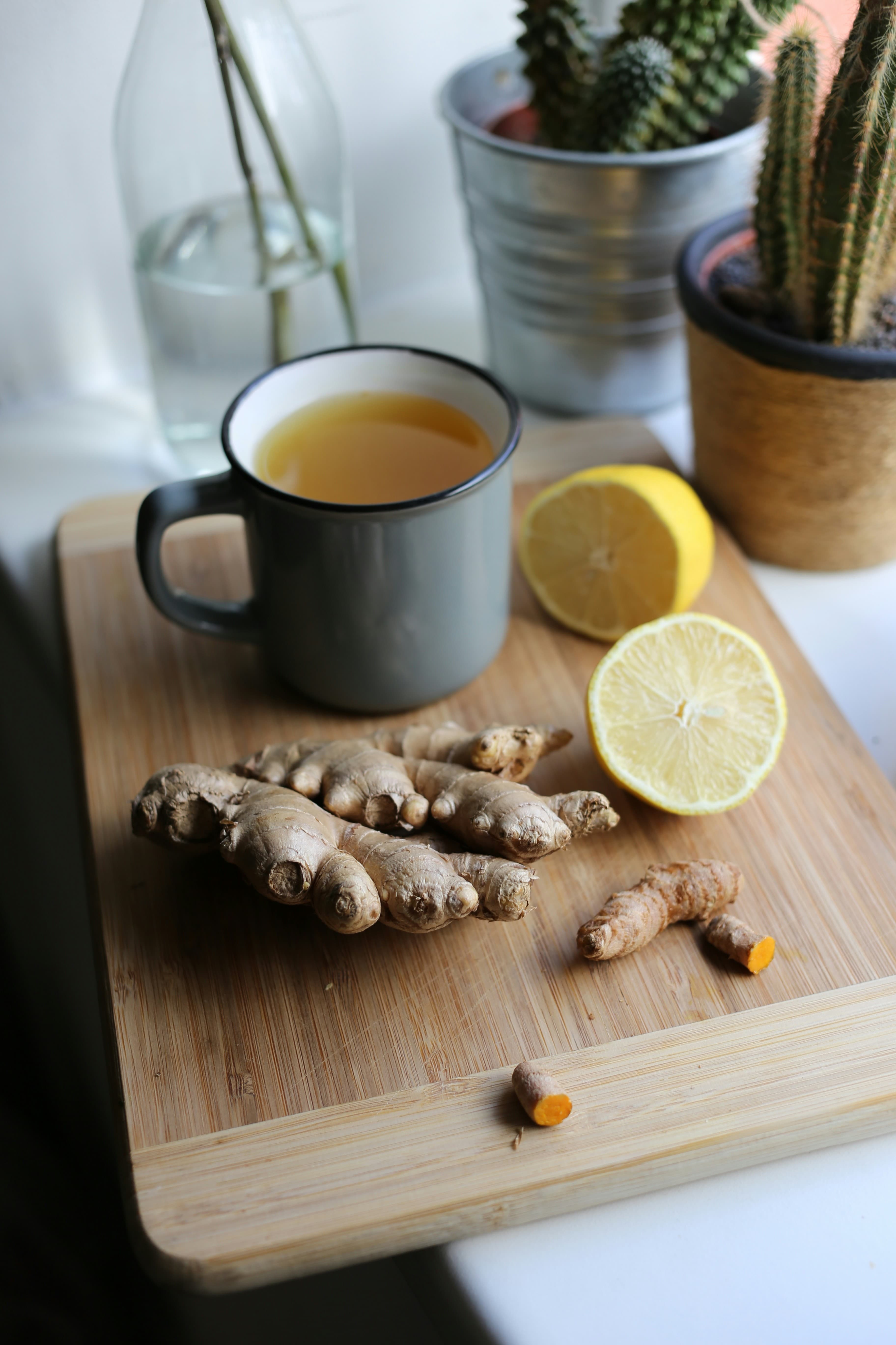 Fresh ginger root and halved lemons on a wooden board beside a mug of hot tea
